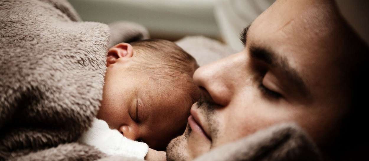 Dad sleeping next to the newborn, both wrapped in a soft blanket